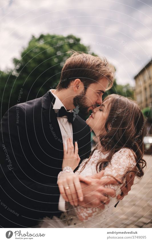 Happy newlywed couple hugging and kissing in old European town street, gorgeous bride in white wedding dress together with handsome groom. wedding day european