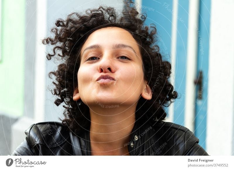 Young attractive woman with curly hair gesturing for a camera selfie and sending kisses. Urban city people concept. young fun cheerful face happy positive