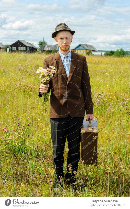 Man hipster with old retro suitcase and wildflowers bouquet man countryside cottagecore vintage summer brown field green jacket rustic travel young male