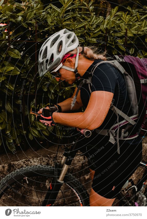 Cyclist on a bike tour looks for the way on her smartphone Mountain bike Nature Landscape Bavaria Helmet Sunglasses sportswear Jersey rest Break Trip Braids