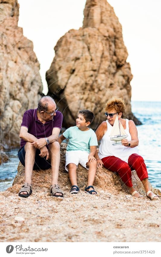 Grandparents and grandson playing with a toy sailboat on the beach boy caucasian child childhood coast coastline cute family grandfather grandmother grandpa
