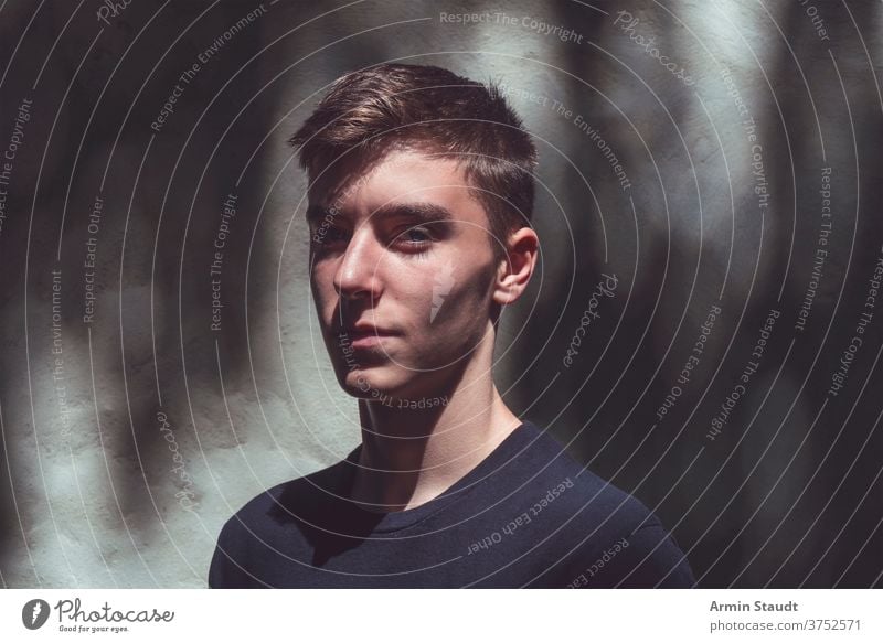 portrait of a self-confident young man standing in the shadow smile mysterious dark sunlight proud closeup wall cool grunge dirt outdoor teenager looking male