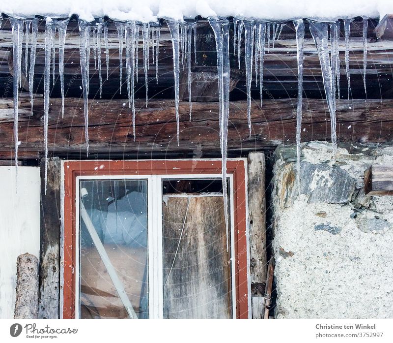 Long icicles hang from the roof of an old hut. Detail view with red window frame, stones and wooden beams Icicle Frost Window Winter Winter mood Ice Stone wall