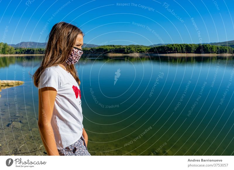 Girl with a white t-shirt and a mask to protecet herself from the coronavirus posing in a lake with the forest reflected in the water cute young caucasian joy