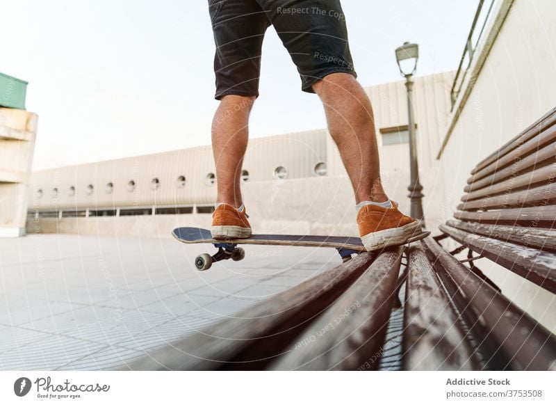 Crop skater doing trick on bench in city skateboard man hobby stunt urban style male skill talent sneakers wooden cool modern summer hipster activity active guy