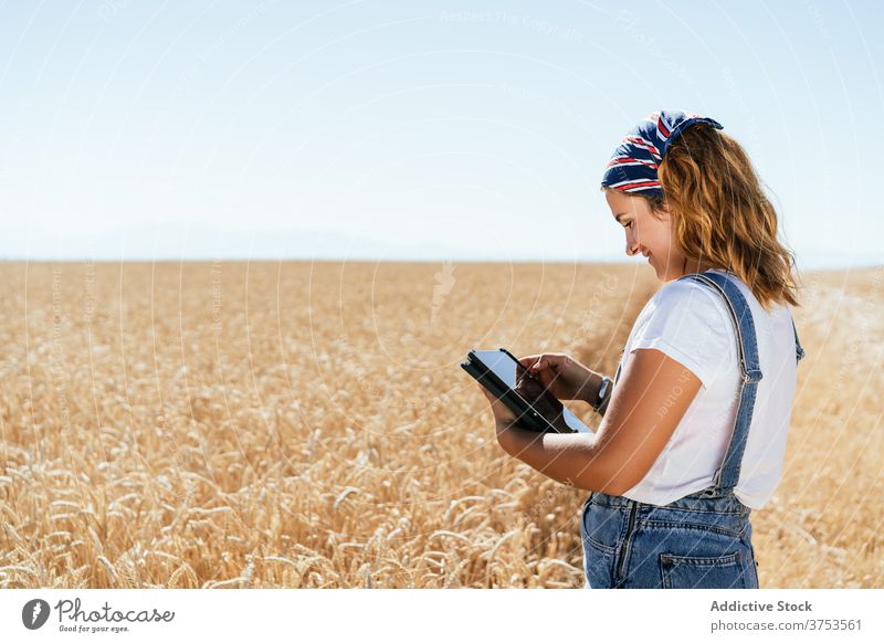 Smiling woman using tablet in field farmer wheat browsing agriculture countryside rural female focus gadget device summer nature meadow plantation farmland