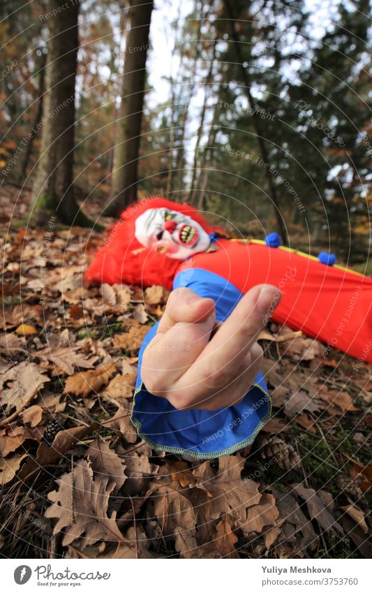 Halloween party. Fuck you. The evil clown gives the finger. Mittle finger gesture. Hallowe'en Party Clown Creepy costume clown overalls Red hair Autumn Forest