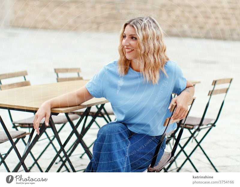 Young women wearing t-shirt and jeans sits in a street cafe girl mockup table round neck apparelmockup casual mock up Seat Person Outdoor Sitting City Portrait