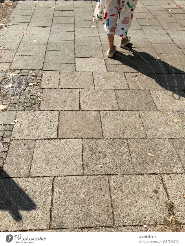 Legs of a woman in a white culotte with colorful geometric shapes on a cobbled pavement. Casting shadows. Walking, pedestrian Fashion garments Geometry