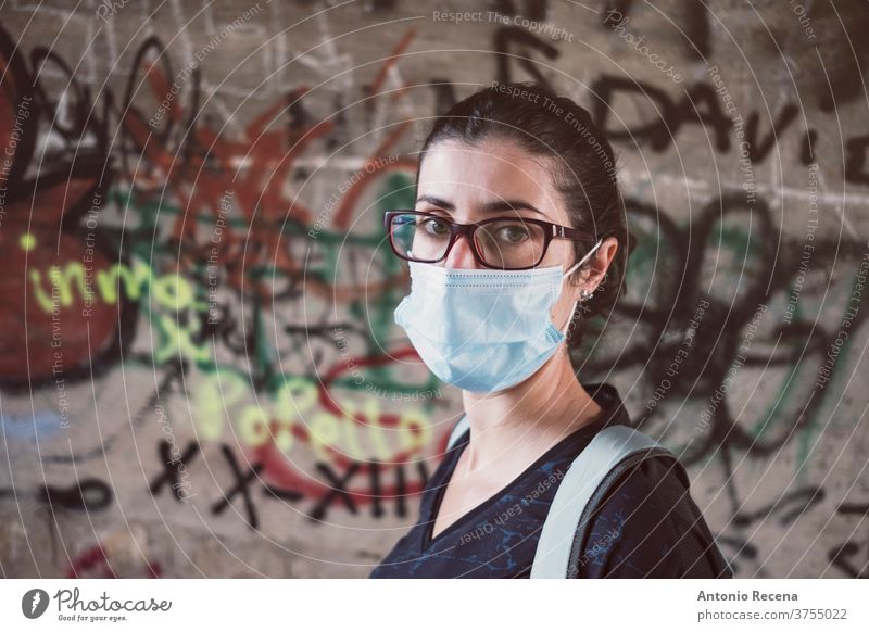 Woman in looking at camera with facial mask in urban photo woman women face mask covid 19 graffiti person people 30s 30-34 years 30-39 years backpack walking