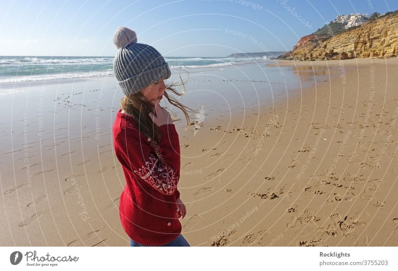 Girl in a bobble hat on the beach in Portugal in winter shore kid fun joy happy caucasian person outdoor travel lifestyle vacation water beautiful algarve alone