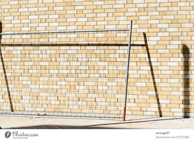 A field of a building fence leans against a wall of clinker bricks and draws a shadow on it Fence Hoarding Construction site Fence field Safety cordon