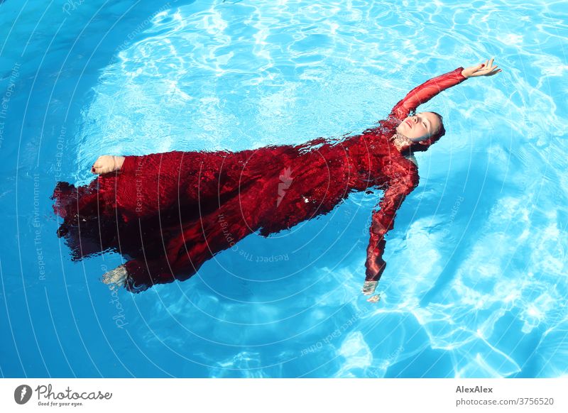 Young woman in a red ball gown lies with outstretched arm in a swimming pool Woman girl already daintily Athletic be afloat Sunlight Summer swimming pools Water