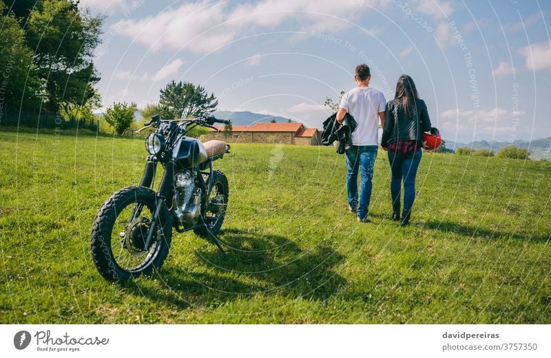 Couple walking on the field holding hands and motorbike unrecognizable backwards couple motorcycle parked trip man motorcycle helmet custom enamored built