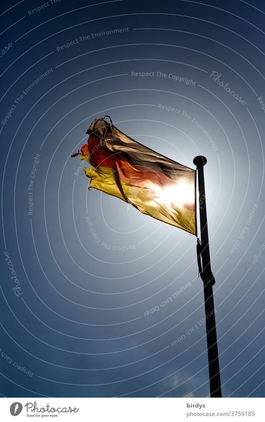 waving, shining German flag with shining through sun shines in the back light before cloudless sky. Germany flag, black-red gold Sun German Flag Wind Blow