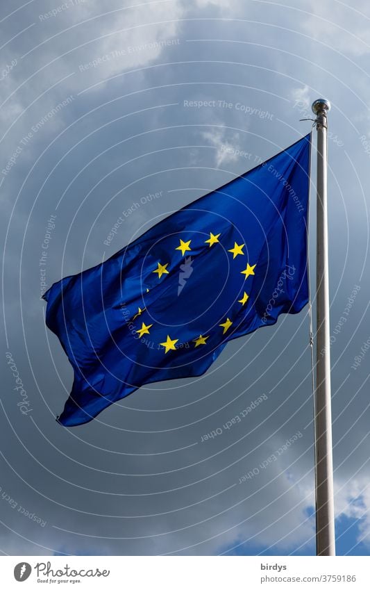 European flag , Flag of the European Union waving in the wind . Thunderclouds in the background Wind waving flag Blue yellow stars identification Pride positive