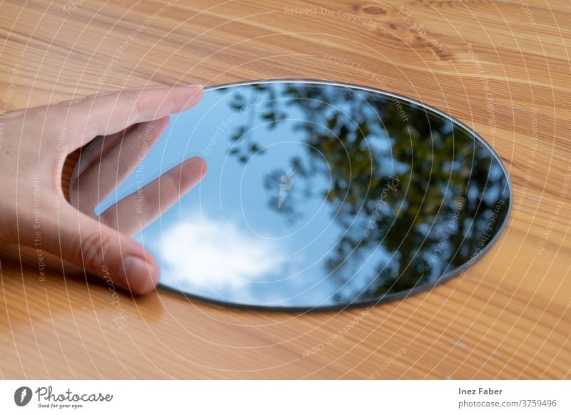 Hand held round mirror on a table, reflection of a tree, clouds and blue sky calm catch the sky cloud reflection tree reflection hand held mirror wooden table
