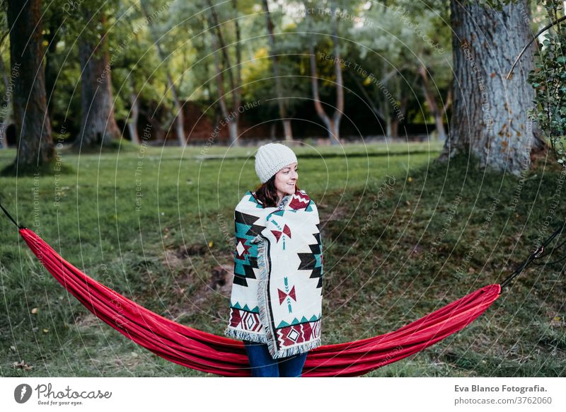 young woman covering with blanket standing next to hammock. autumn season. camping concept cold outdoors nature sunset orange park caucasian preparing relax