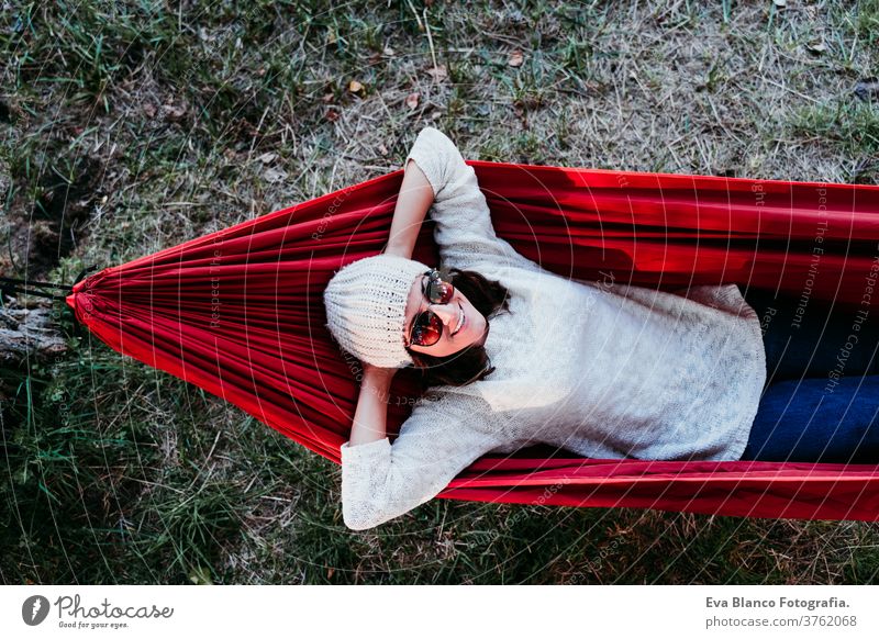 young woman relaxing in orange hammock. Camping outdoors. autumn season at sunset lying nature park caucasian preparing happy campground morning light