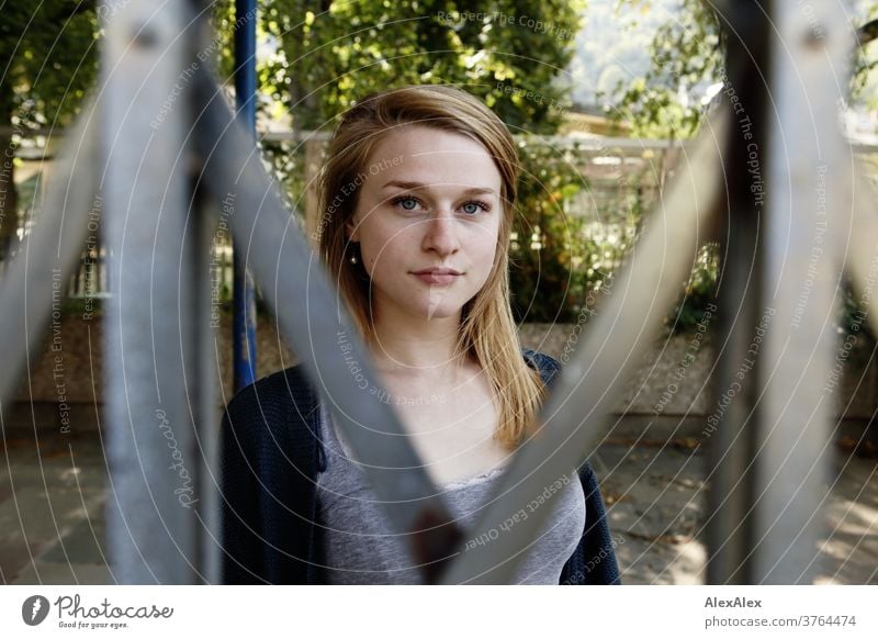 Close portrait of a young woman standing behind a sliding gate and looking through it Woman Young woman Slim already athletic Blonde youthful 18-25 years