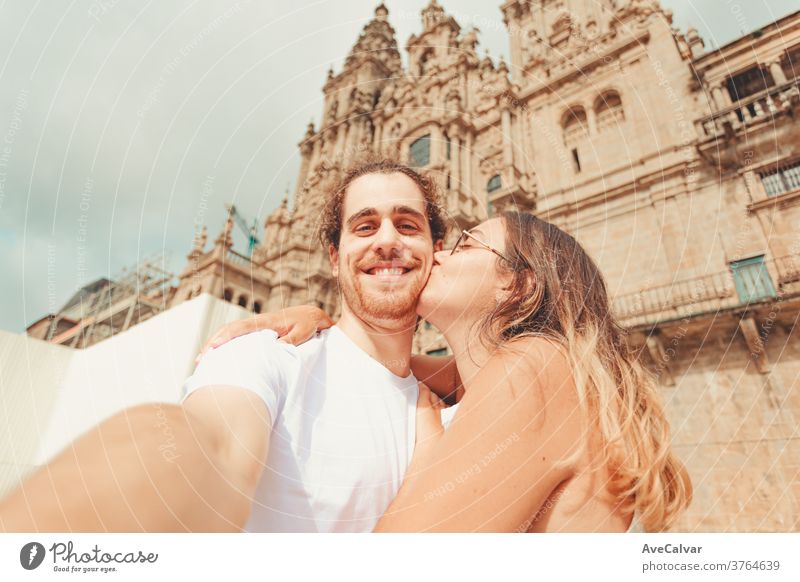Young man taking a selfie and smiling while his girlfriend kisses him adult feeling white fun portrait pose woman hugging boyfriend young couple hold happiness