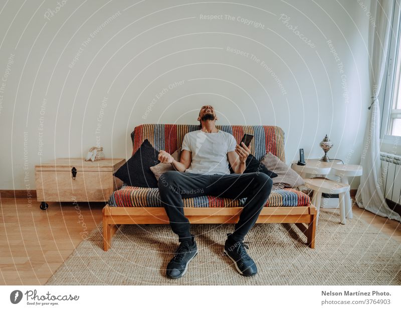 Hispanic man siting on the couch. He is laughing with his smartphone in his hand. 1 freedom adult looking casual attire lifestyle holiday vacation latin alone