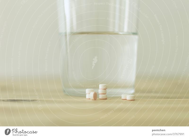 Several tablets piled up are lying on a table in front of a drinking glass filled with water. Sickness, medication. Addiction to pills. medicine Tumbler Illness