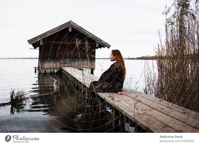 Lonely woman standing on wooden pier at lake shed autumn gloomy lonely traveler shabby calm tranquil nature female tourism germany austria water gray cloudy