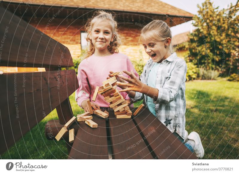 Two girls are having fun and playing a wooden board game outdoors near their home. children leisure development tree sister three happy cube useful smart family