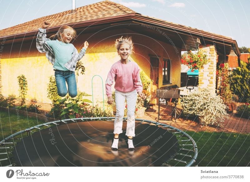 Happy two blonde girls are jumping on a trampoline in the garden near their house. Leisure and games children together happy childhood caucasian summer fun