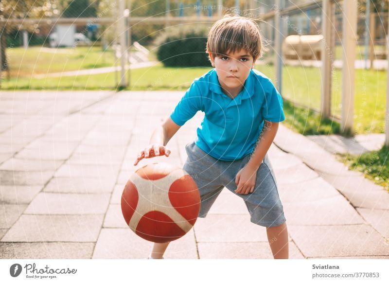 Focused cute boy athlete leads the ball in a game of basketball. A boy plays basketball after school. Sports, healthy lifestyle dribbling sport player male