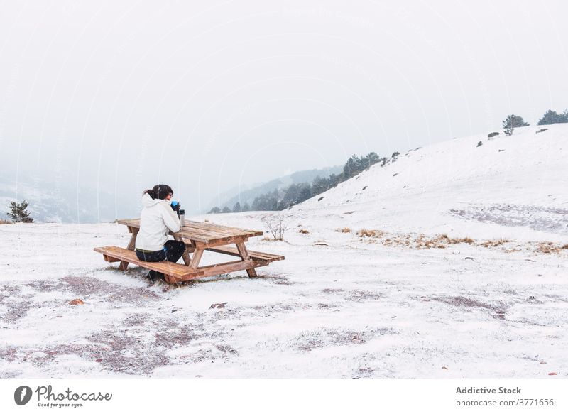 Unrecognizable tourist sitting on bench in mountains in winter traveler hot tea enjoy snow landscape tourism amazing pyrenees catalonia spain thermos table