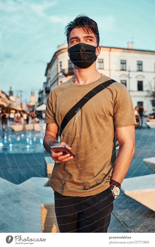 Young man standing in the city center wearing the face mask to avoid virus infection caucasian conversation covid-19 lifestyle outbreak outdoors pandemic