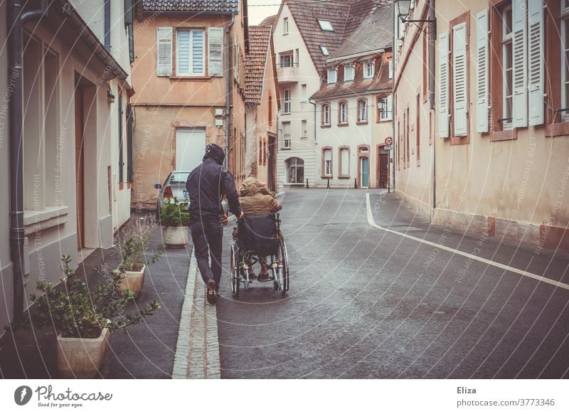 A man pushes a disabled person in a wheelchair down the street Wheelchair handicap Mobility Health care Rainy weather Illness Trip Push walking impediment