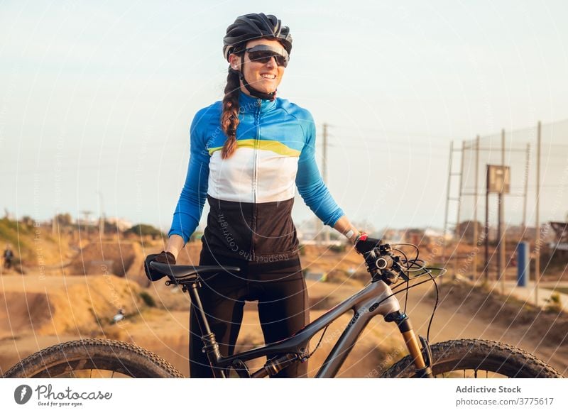 Sporty young woman in helmet with bicycle looking at camera smiling mountain bike trial cyclist trick sportswoman biking cycling sportswear riding glasses