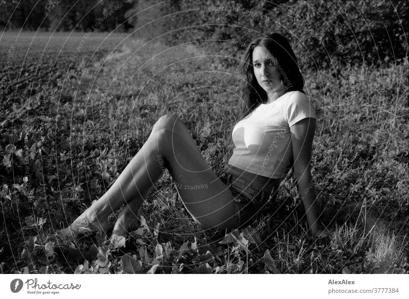 Black and white portrait of a young woman sitting in the grass in front of a forest at the edge of a field Woman already Near fit daintily Skin Face Blonde look