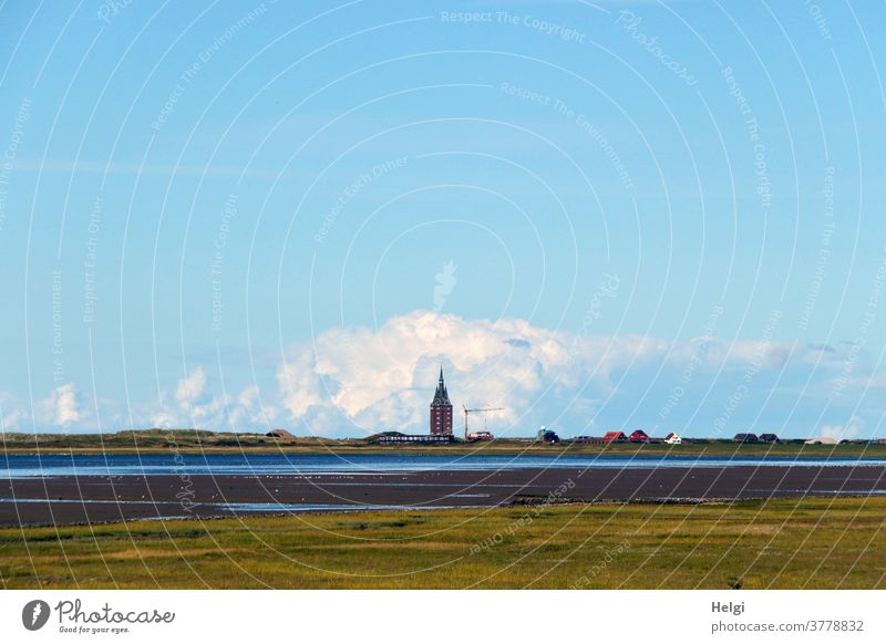 Low tide in the mudflats - view over salt marshes and the Wadden Sea to the west tower of Wangerooge, behind which a thick cloud piles up in front of a blue sky