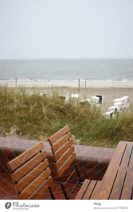 rainy day - empty wet chairs stand at the table on the beach promenade with a view of the beach with beach chairs and the rough North Sea Table dune Beach Sand