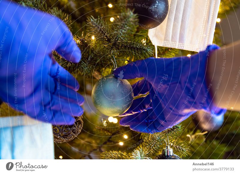 Person decorating a beautiful Christmas Tree with protective safety gloves for Covid-19, Concept for Coronavirus and Christmas Holiday hanging happy celebrating
