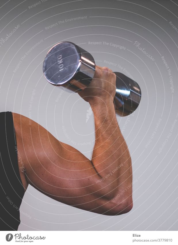 A muscular man with trained upper arms lifts a 10 kilo dumbbell. Focus on the biceps. Man Dumbbell chiselling Muscular Sports weight training Force Upper arm