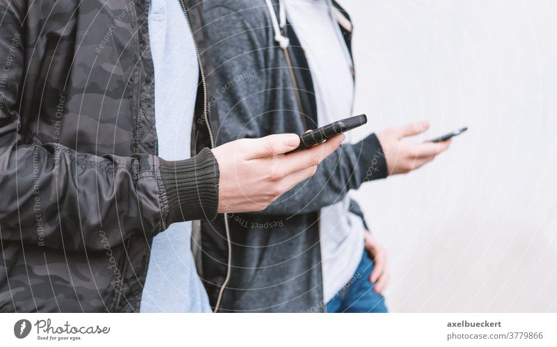 two unrecognizable mobile phone addicted male teenagers using smartphone antisocial millennials young men friends cell cellphone technology media network