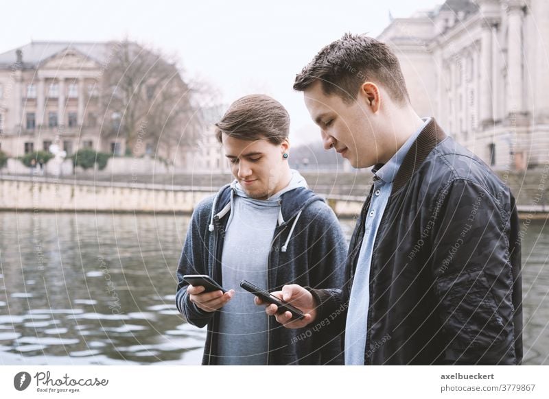 two mobile phone addicted male teenagers standing together looking at smartphone antisocial millennials young men friends using cell cellphone technology media