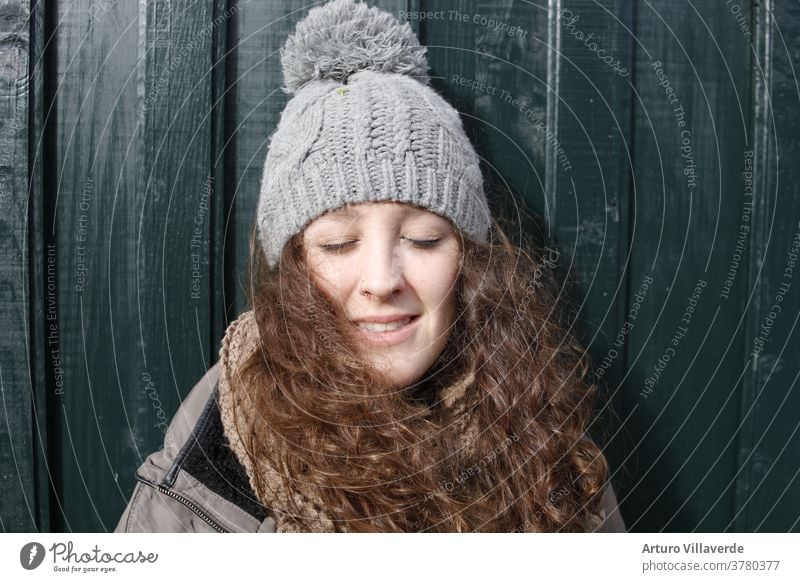 portrait of a girl with closed eyes, long hair and a gray cap leaning against a green wooden door isolated white smile caucasian studio lady face childhood cute