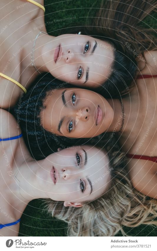 Happy multiracial women lying together on grass face to face friendship serious carefree young friendly freedom multiethnic diverse african american black