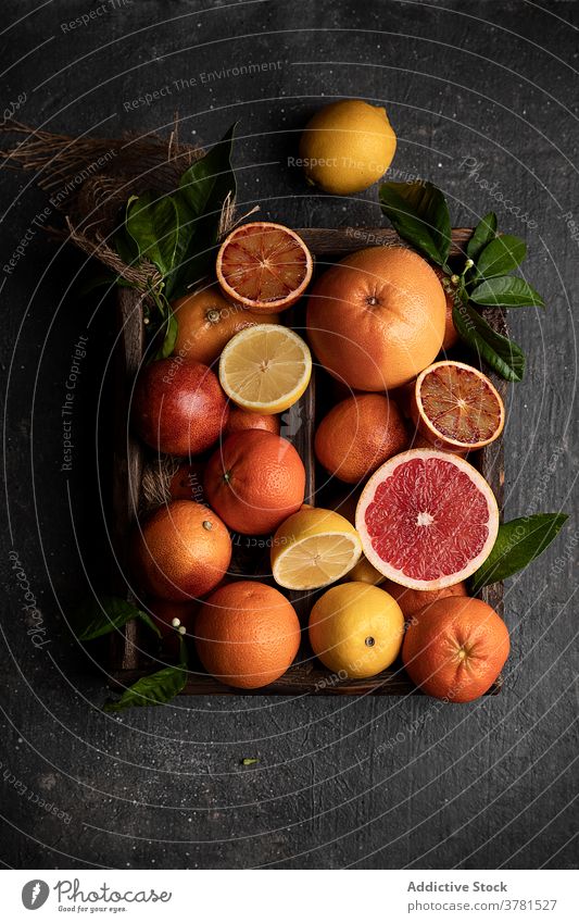 Assorted citruses arranged on black table fruit various ripe fresh lemon orange grapefruit tangerine wooden tray green leaf arrangement organic vegetarian