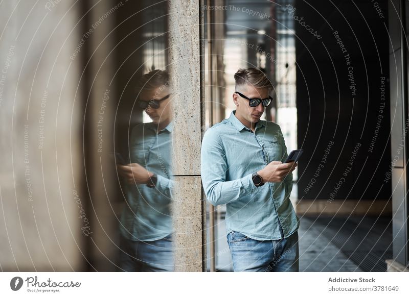 Serious man using smartphone in city style browsing handsome trendy masculine chat male apparel attire urban communicate gadget device street casual modern