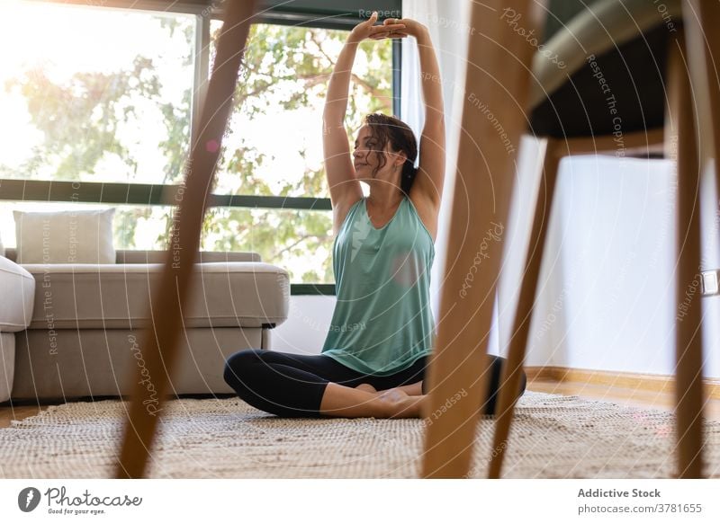 Serene woman doing yoga on floor at home practice flexible lotus pose legs crossed padmasana stretch female peaceful sportswear wellness carpet room harmony