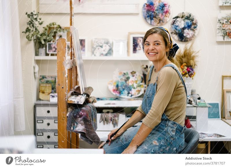 Happy craftswoman painting on easel in workshop artist canvas happy cheerful creative draw smile talent female colorful picture hobby inspiration artwork