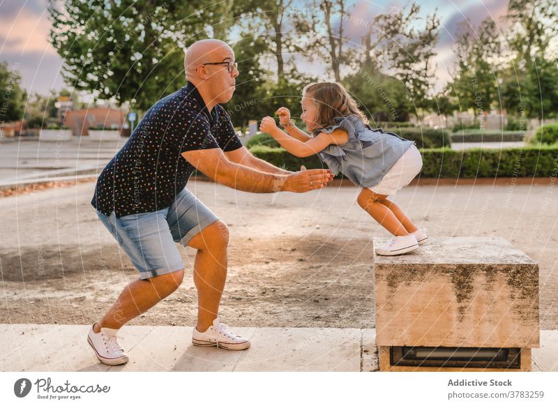 Man playing with girl in park in summer father daughter having fun together playful jump catch entertain city kid child bonding parent cheerful joy stone