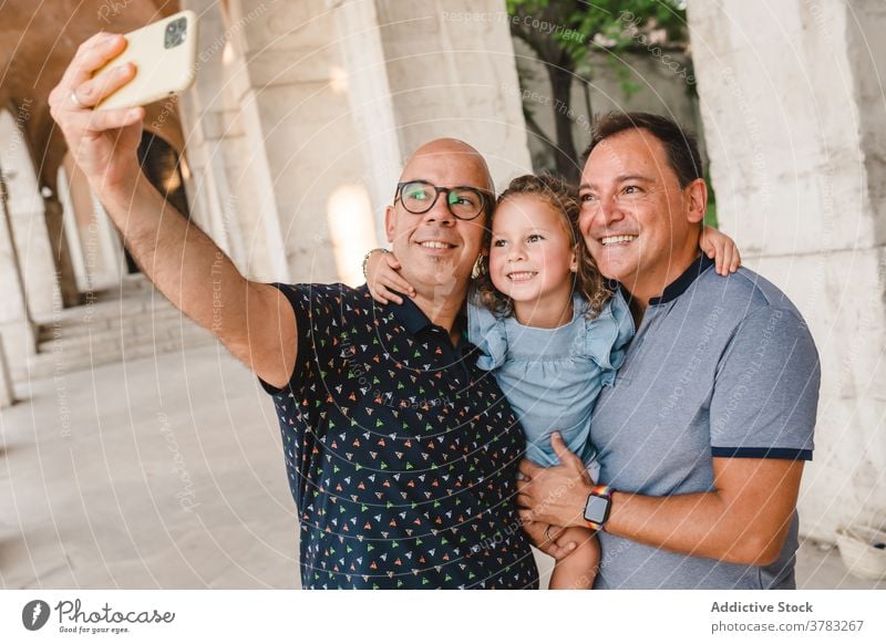 Cheerful LGBT family taking selfie in city lgbt child couple gay men girl smartphone homosexual together take photo self portrait cute daughter street smile